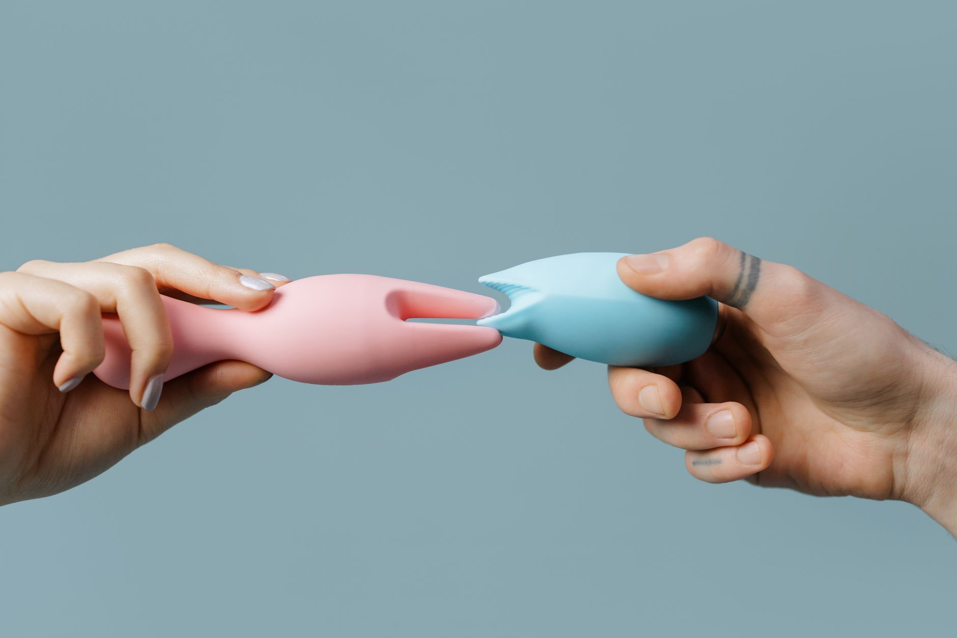 Hands holding colorful silicone sex toys against a neutral background
