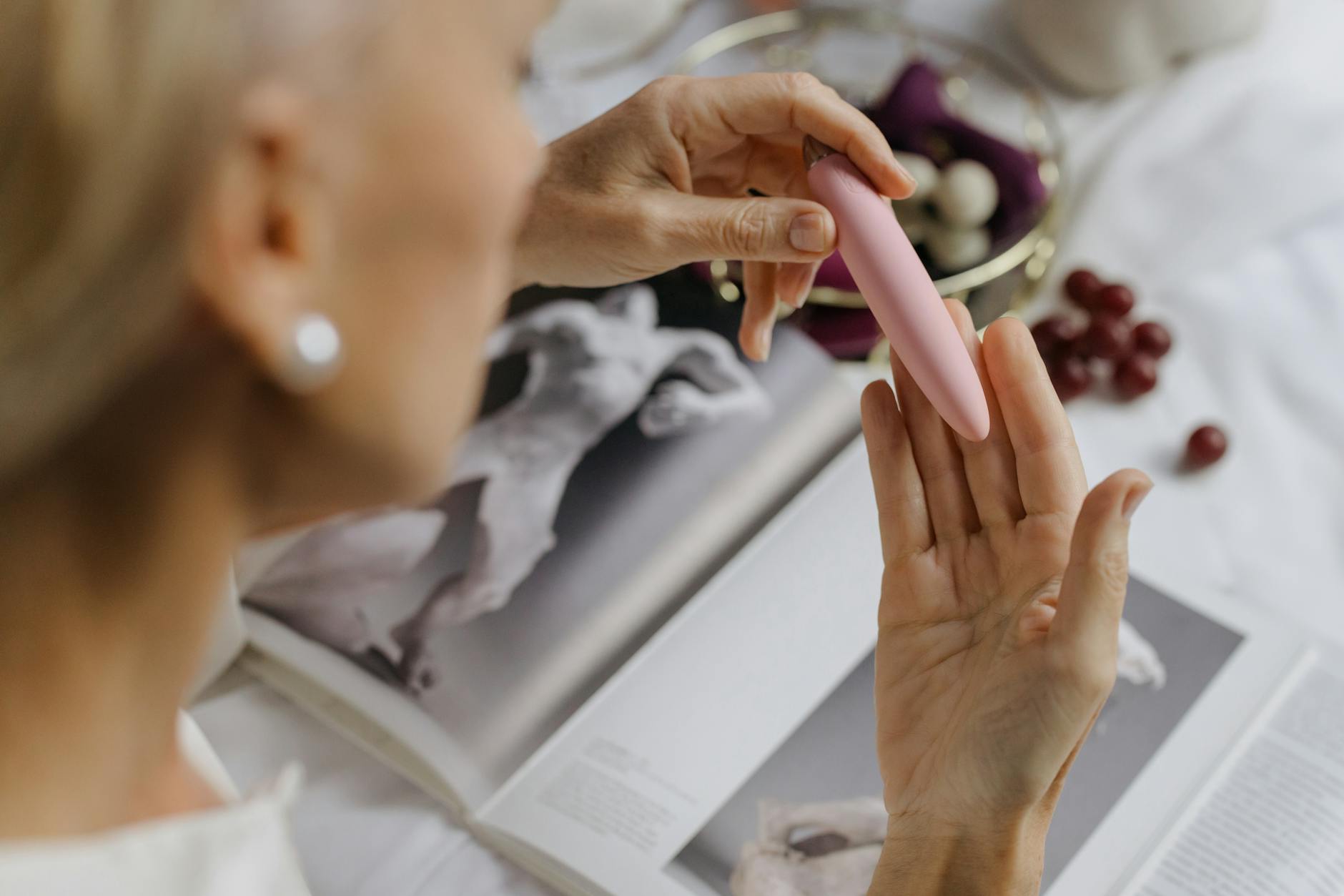 Close-up detail of a woman's hand holding a pink vibrator near personal items, emphasizing mindful pleasure and intentional self-care.