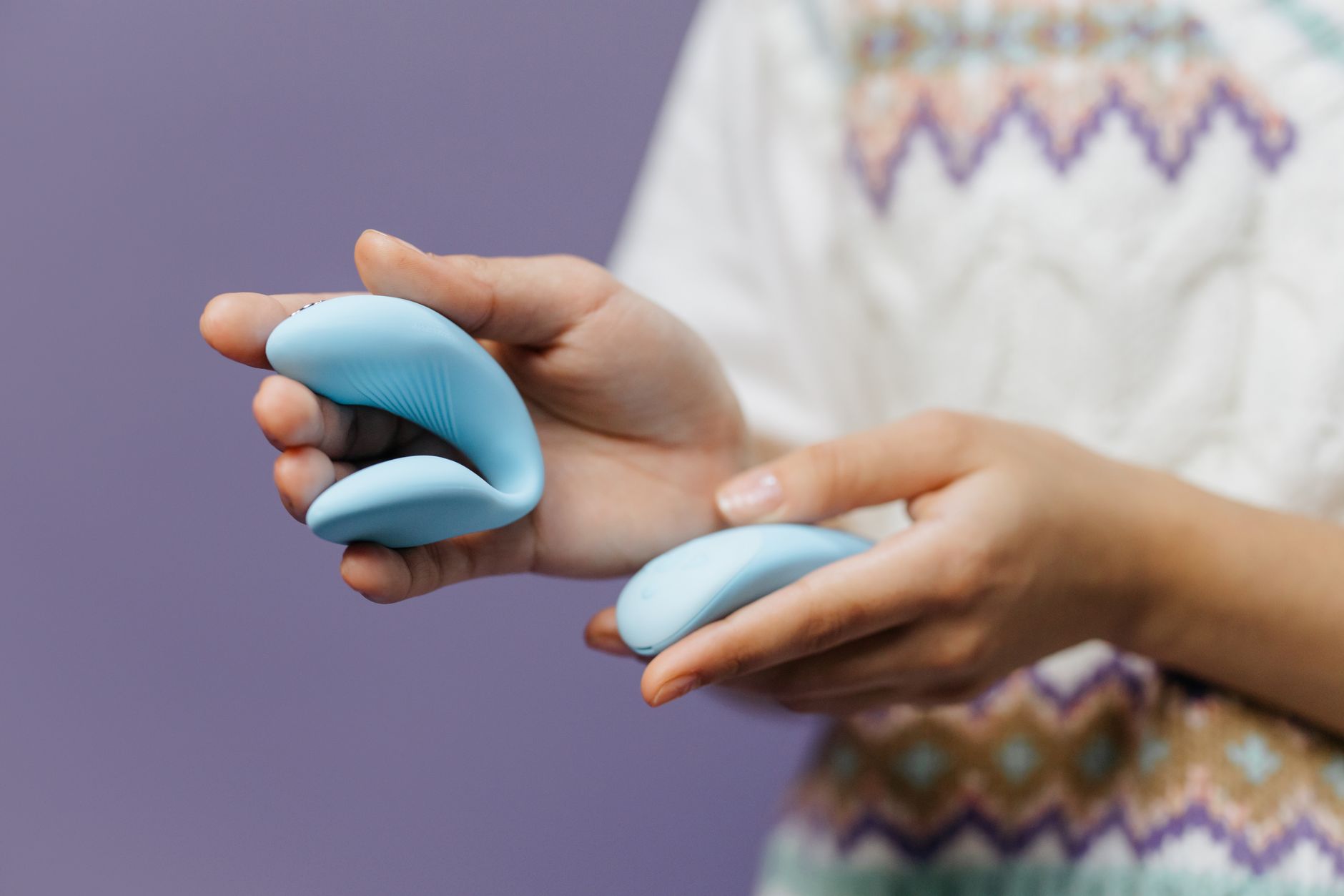 Two hands holding a sleek vibrator together against a purple background, symbolizing shared pleasure.