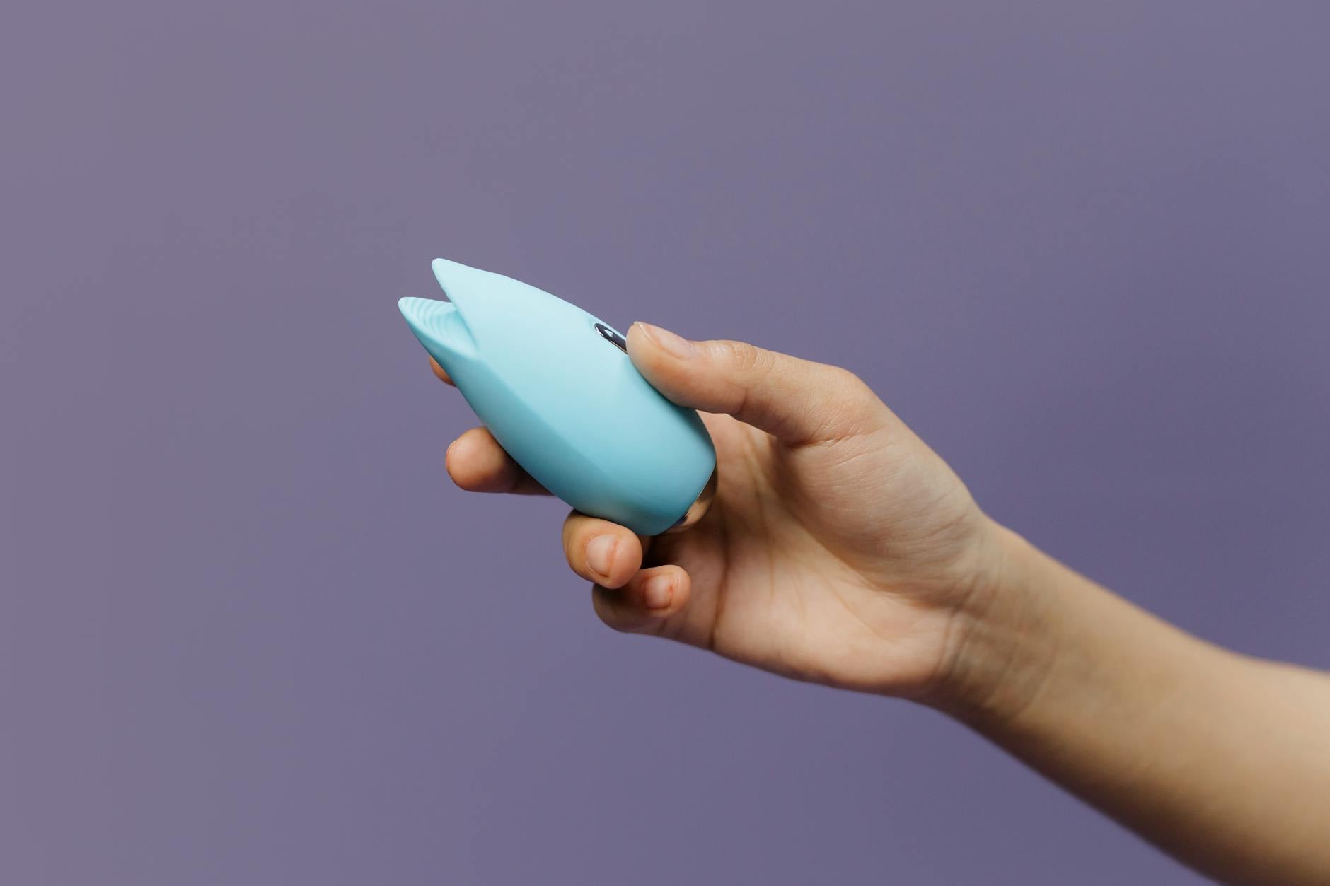 Person holding a blue silicone vibrator against a purple background
